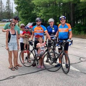 Attorney Scott T. Lever stands in a group if individuals outside on a sunny day. Scott is prepared to race on his bicycle. 